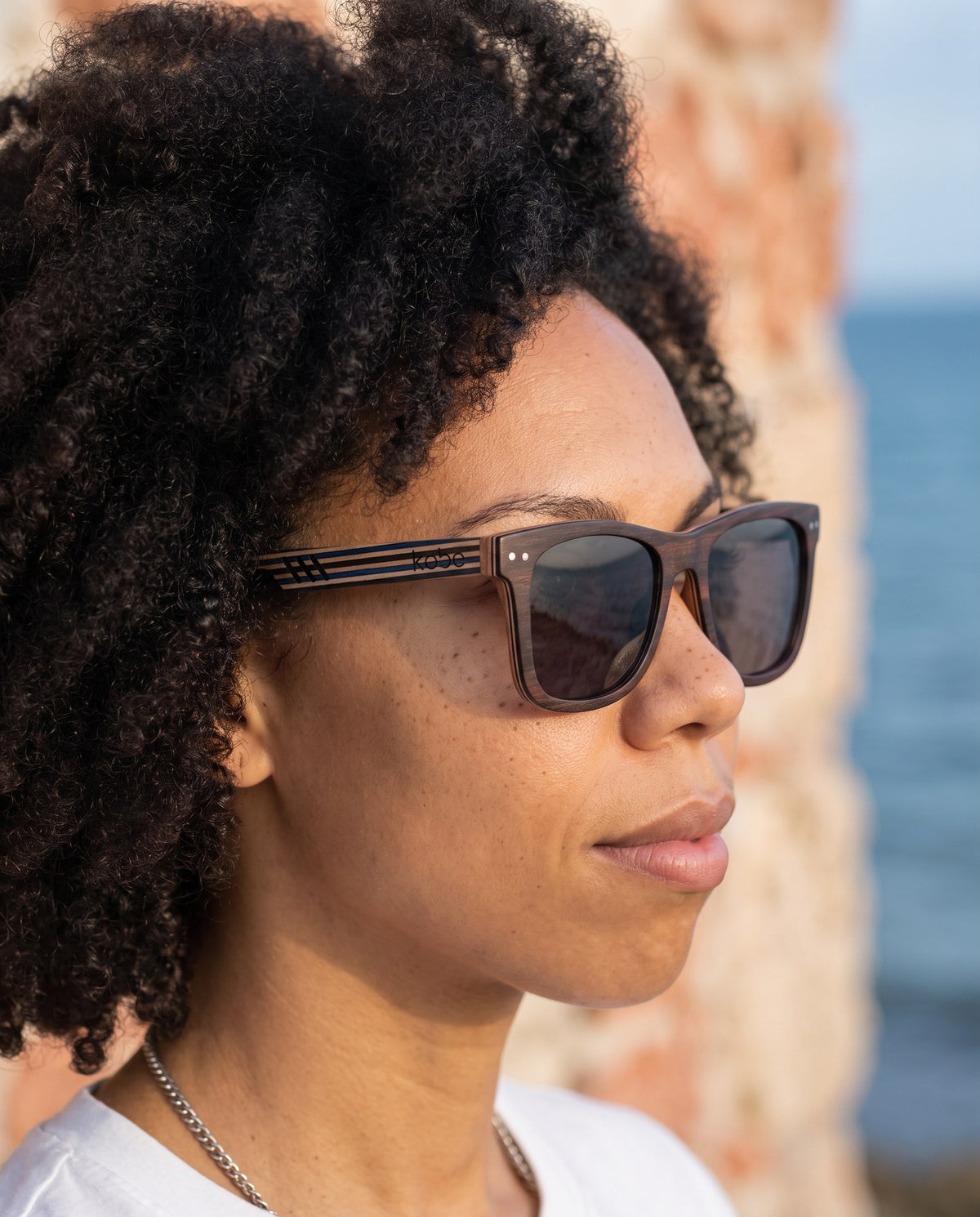 Woman wearing Borneo Skate Blue sunglasses by Kobe Afrika by the water, close-up