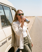 Woman taking a water stop by a Land Cruiser on a desert road in Chalbi Green sunglasses by Kobe Afrika