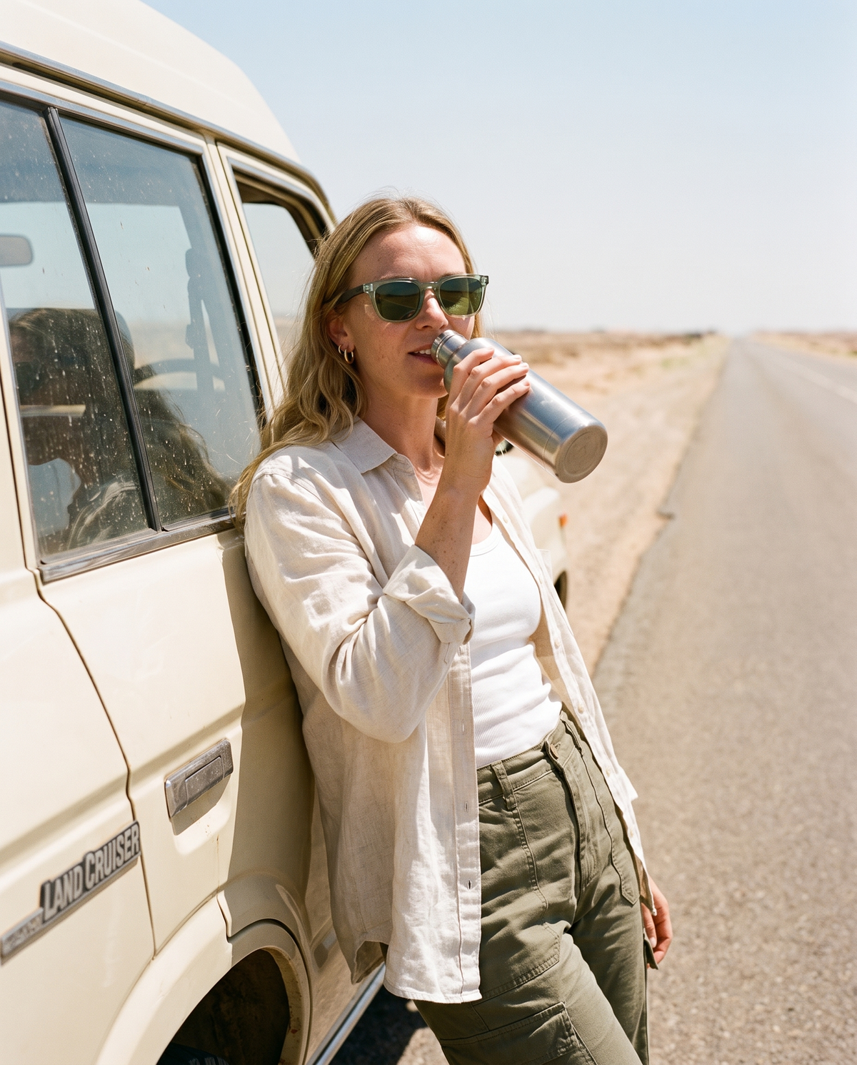 Woman taking a water stop by a Land Cruiser on a desert road in Chalbi Green sunglasses by Kobe Afrika