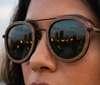 Close-up of Kyzyl Walnut sunglasses by Kobe Afrika on a woman, city lights in the lens
