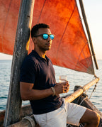 Man sitting on a dhow under a red sail in Oahu Ocean sunglasses by Kobe Afrika